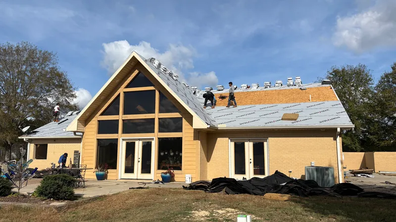 An A-frame brick home partway through a roof replacement, crew on the roof