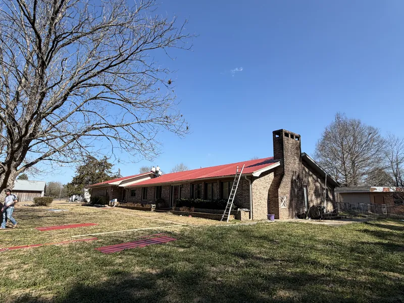 A long brick ranch house with a new red metal roof and a tall brick chimney
