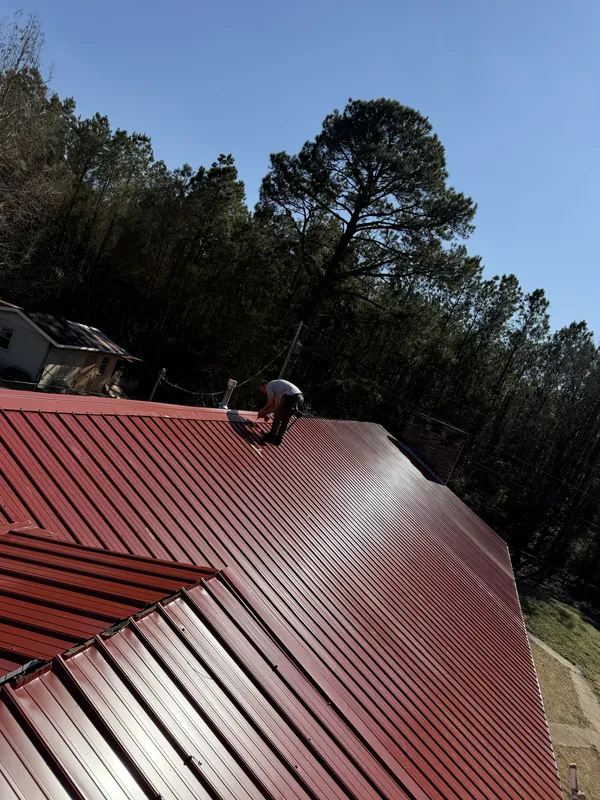 A roofer working along the ridge of a new red metal roof
