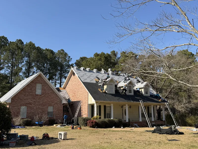 A crew laying shingles over new underlayment on a brick house with three dormers