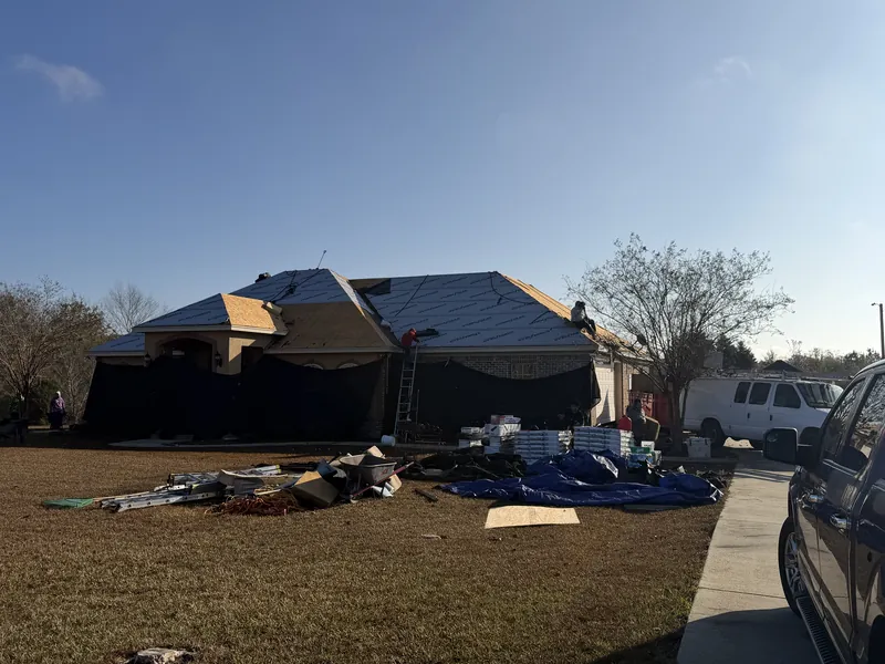 Synthetic underlayment across a whole roof, with a crew on top and materials on the lawn